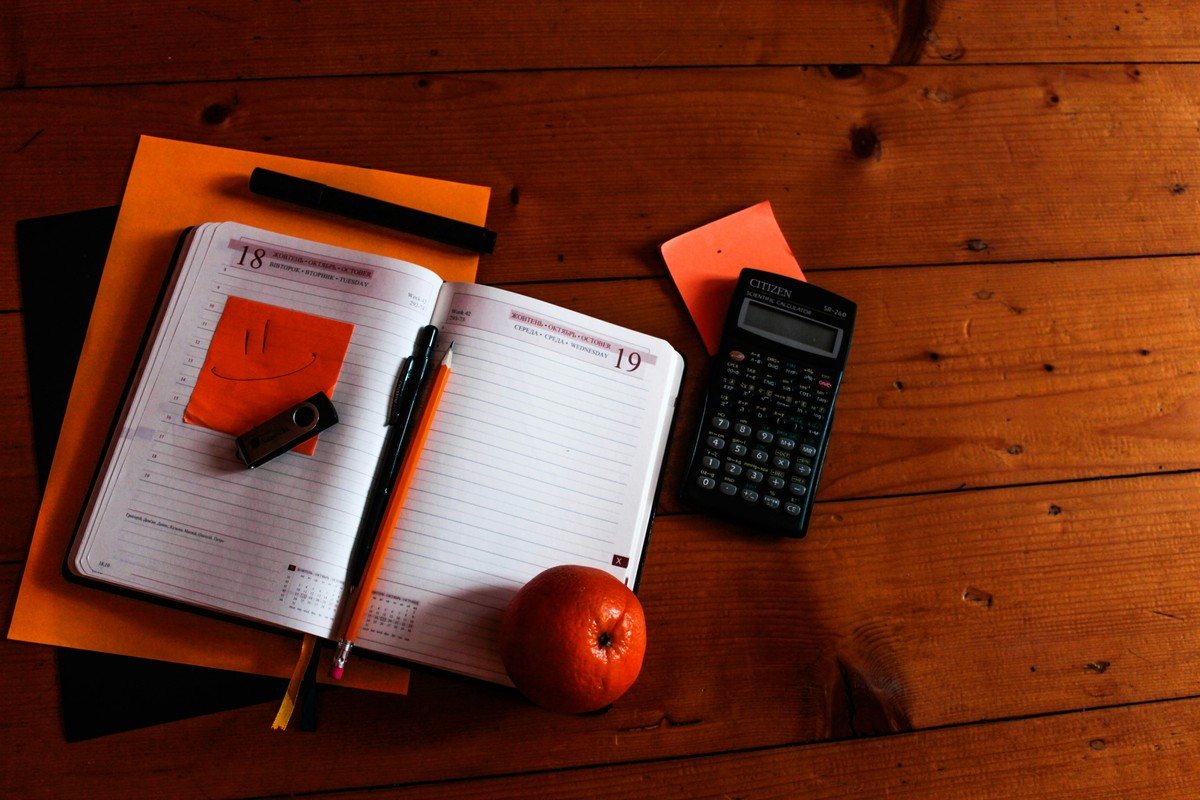 Agenda ouvert, calculatrice et carnets posés sur un bureau en bois pour un suivi mensuel